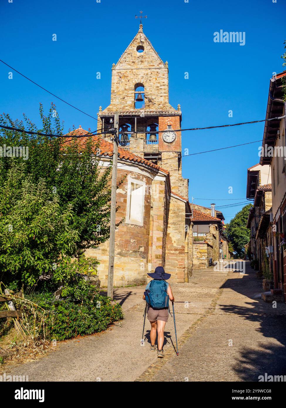 Un pèlerin avec des bâtons de randonnée marche vers l'église Iglesia de la Asuncion à Rabanal del Camino, un arrêt clé sur le Camino de Santiago. Espagne Banque D'Images