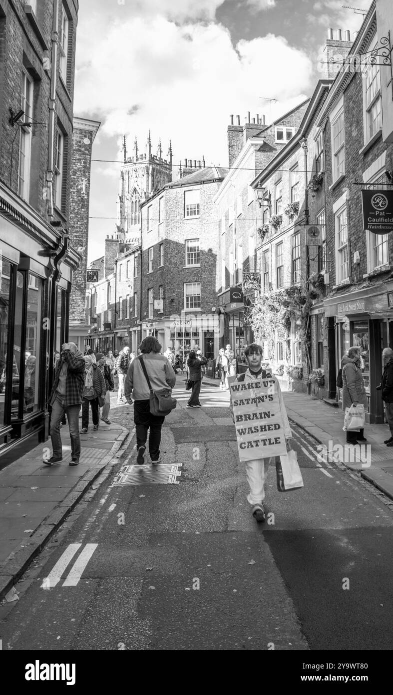 Homme marchant le long des rues étroites avec un panneau de protestation et habillé de blanc dans la ville acient de York. Banque D'Images