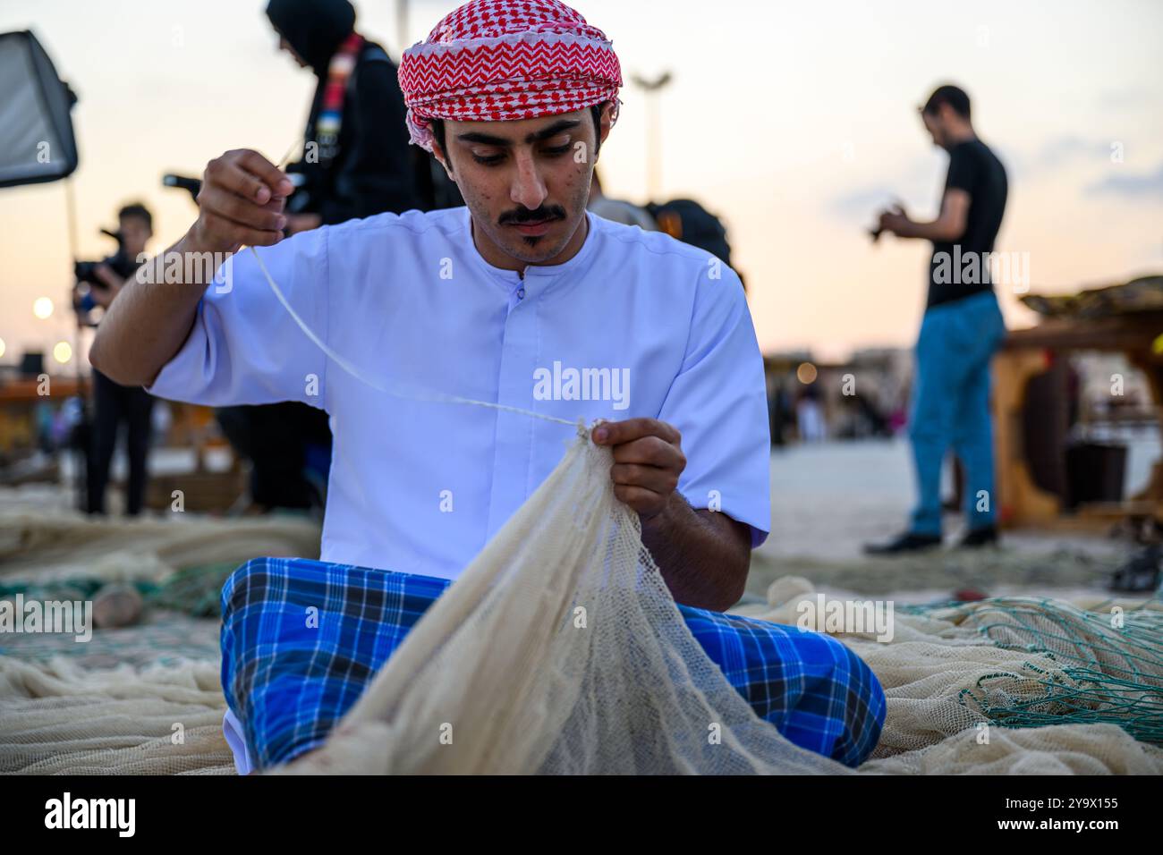 Doha, Qatar - 29 novembre 2023 : un homme arabe répare un filet de pêche pendant le festival des roulements à voile dans le village de Katara. Banque D'Images