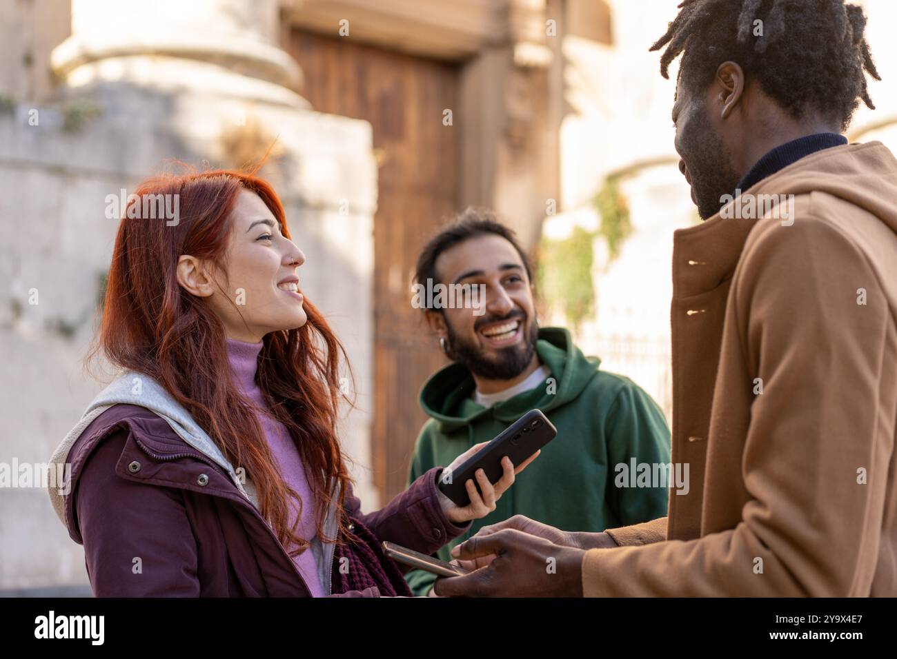 Heureux amis divers interagissant à l'extérieur. Groupe multiculturel de jeunes adultes utilisant des smartphones et socialisant en milieu urbain. Concept de Friendsh Banque D'Images
