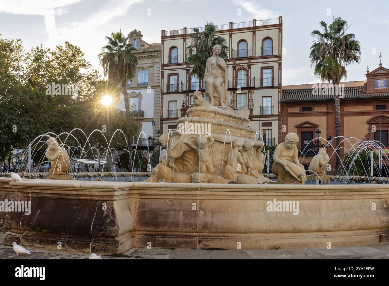 Fontaine historique avec des statues devant un bâtiment et des palmiers à la lumière du soleil, Séville Banque D'Images Fontaine historique avec des statues devant un bâtiment et des palmiers à la lumière du soleil, Séville Banque D'Images