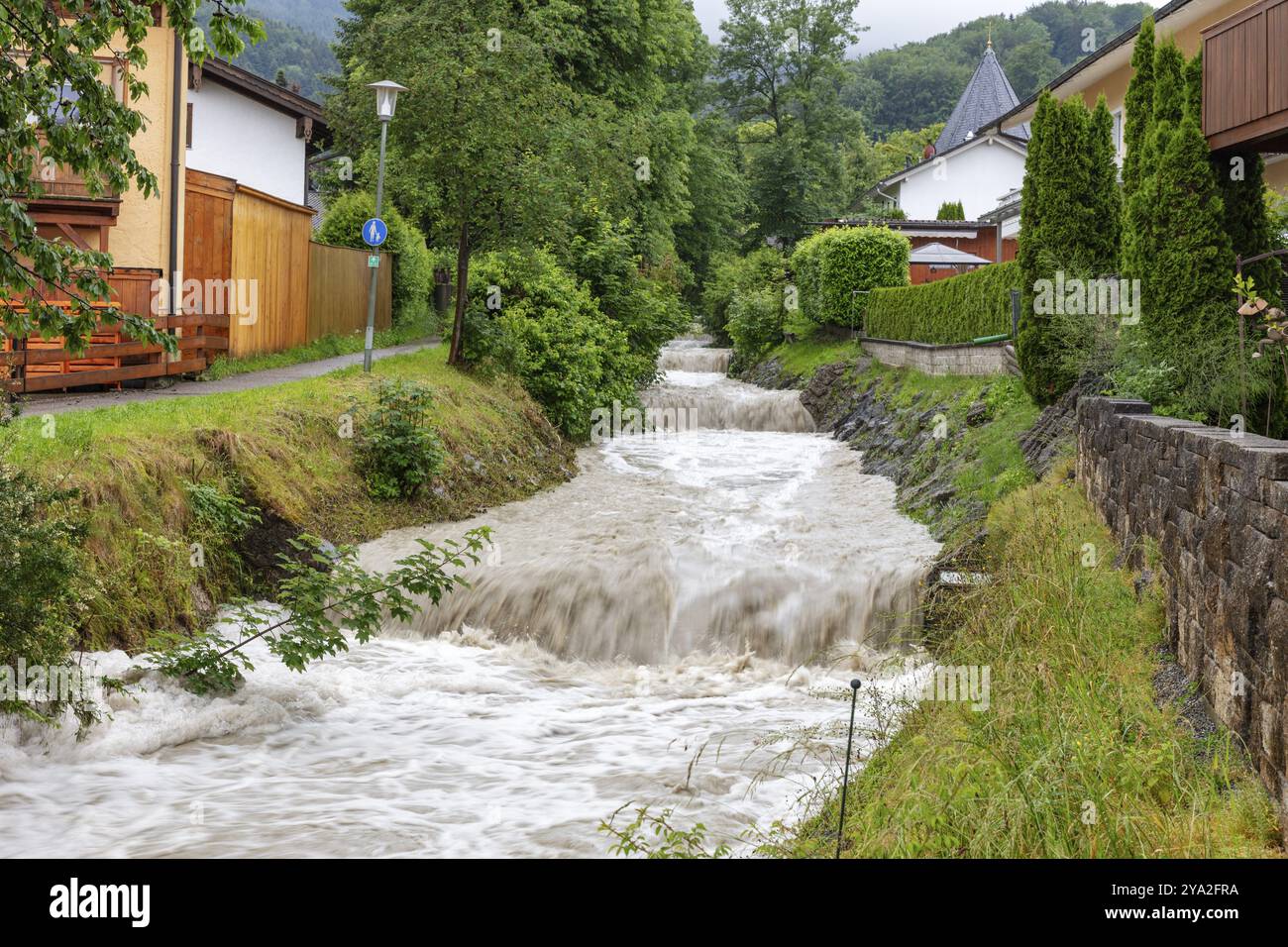 Petit ruisseau dans un quartier résidentiel avec un fort courant, entouré d'arbres verts et de maisons, Osterbach, Bad Feilnbach Banque D'Images Petit ruisseau dans un quartier résidentiel avec un fort courant, entouré d'arbres verts et de maisons, Osterbach, Bad Feilnbach Banque D'Images