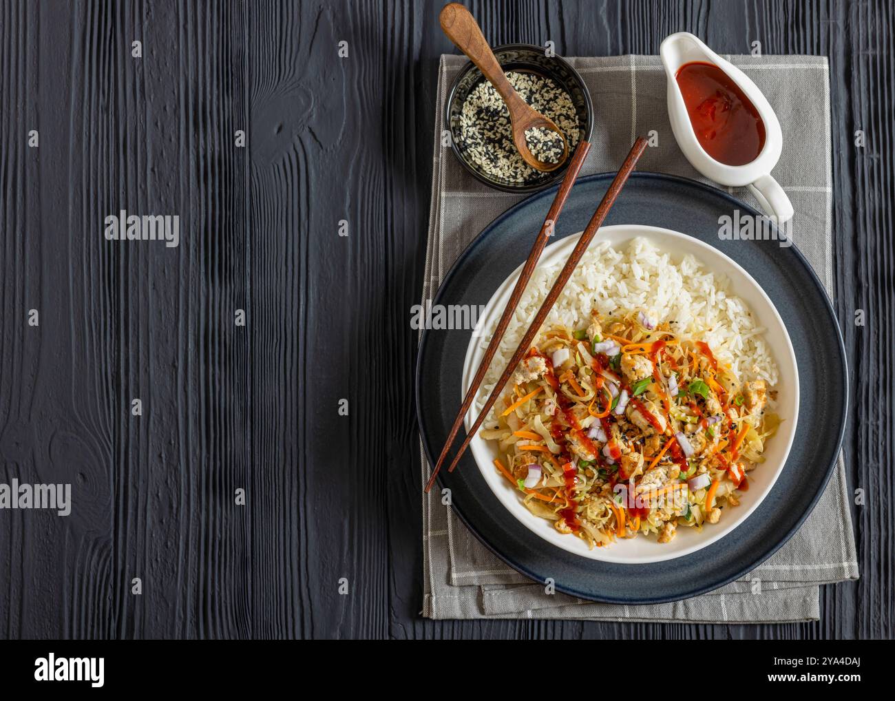roulé aux œufs de tofu, chou sautés, tofu émietté assaisonné servi dans une sauce sucrée et salée servie sur du riz dans un bol sur une table en bois noir avec chopsti Banque D'Images