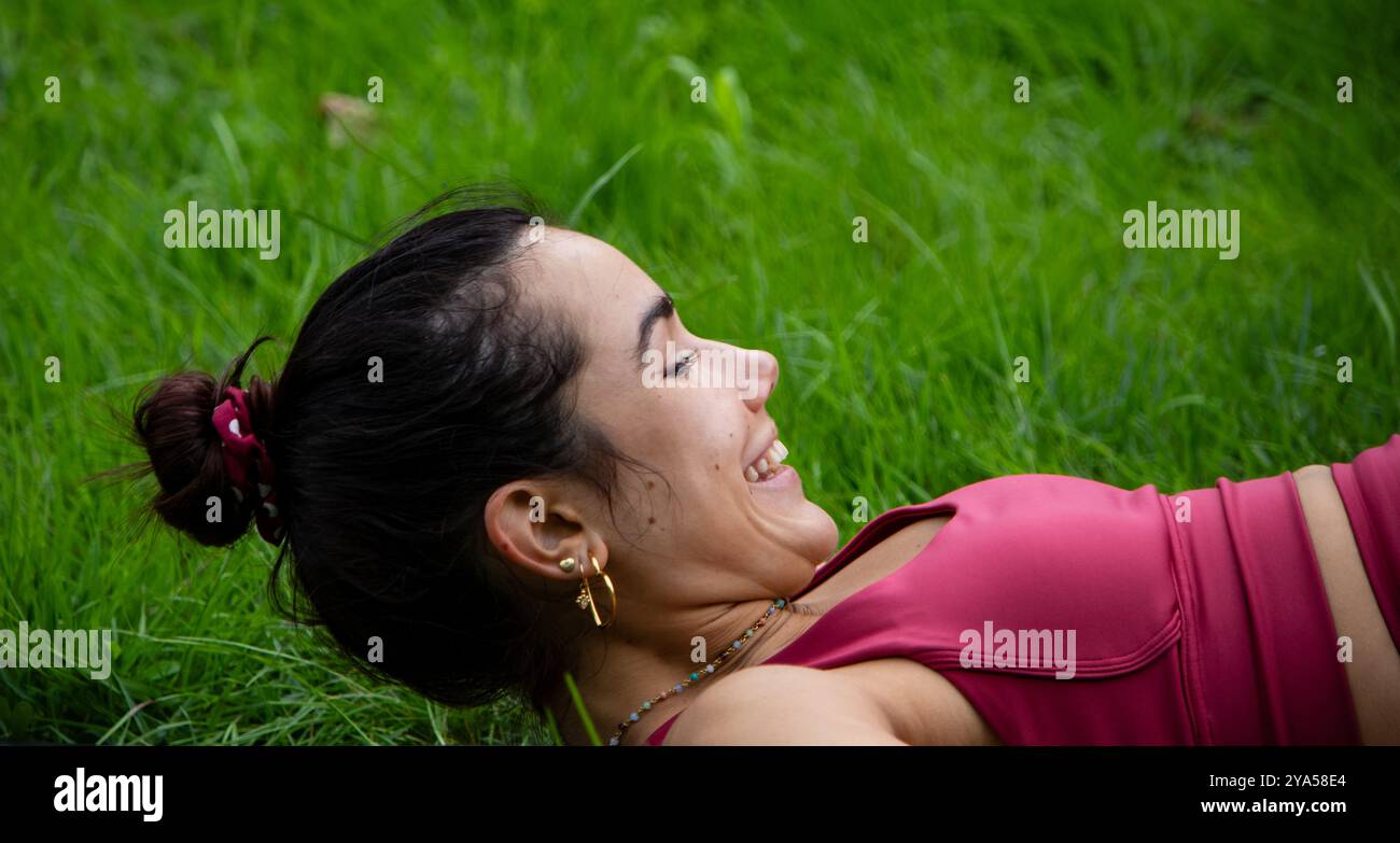 Gros plan d'une belle jeune femme s'amusant et riant tout en pratiquant le yoga sur un fond vert de la nature avec ses cheveux attachés en arrière Banque D'Images