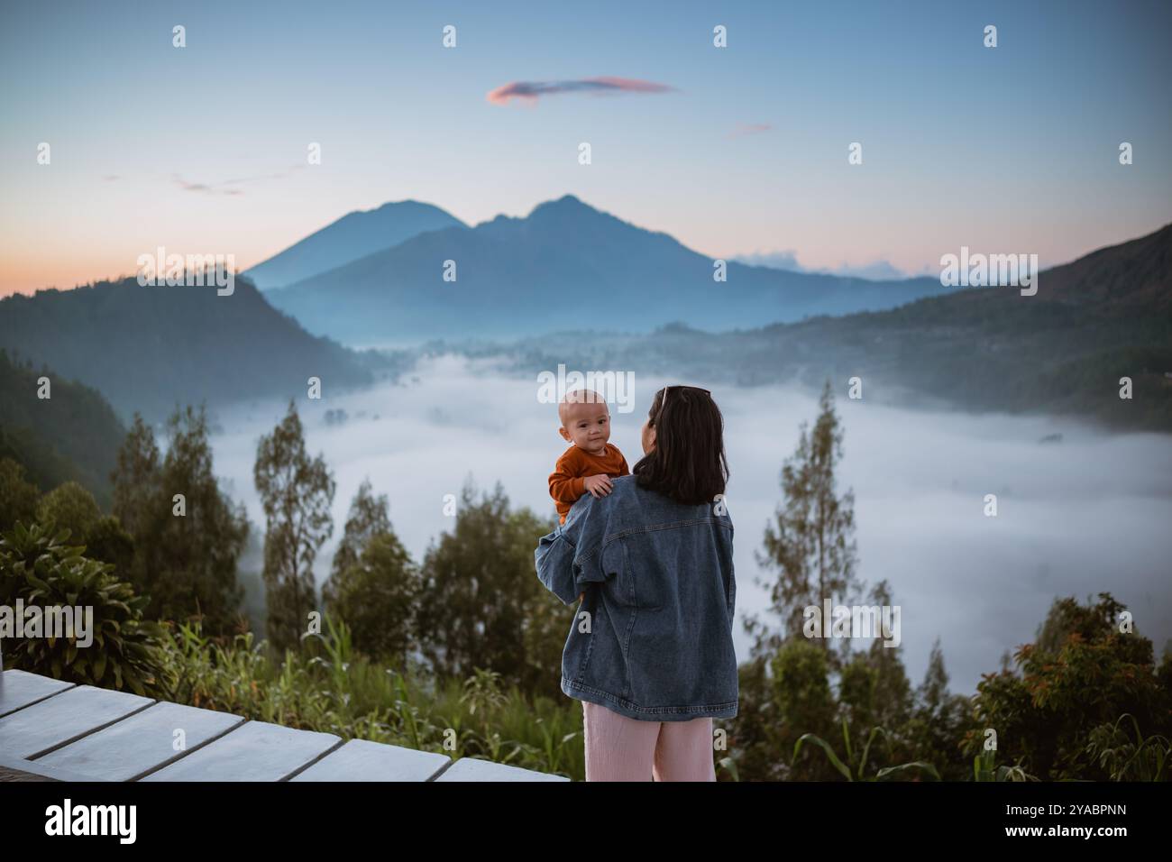 Mère et enfant appréciant un lever de soleil serein de montagne avec paysage brumeux Banque D'Images