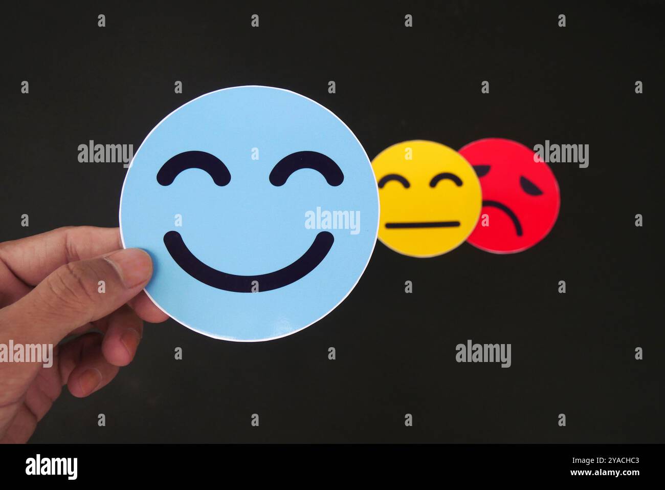 Main tenant la carte visage triste caché derrière visage heureux. Concept de sautes d'humeur, bipolaire, dépression, dépression, santé mentale, personnalité multiple et a Banque D'Images