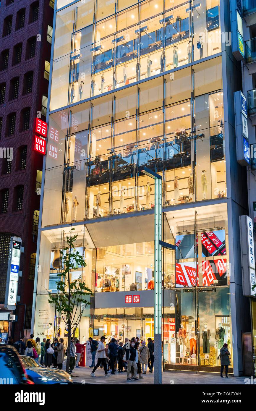 Soirée de l'autre côté de la rue vue de l'entrée du magasin phare Uni Qlo à la mode sur le Ginza. Mannequins habillés dans les vitrines. Banque D'Images