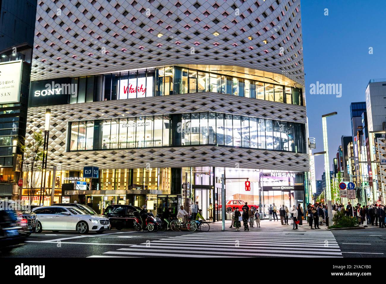 Vue de l'autre côté de la rue de la salle d'exposition de voitures Nissan dans le bâtiment Ginza place revêtu de blanc sur la Ginza. Dans la circulation avant attendant au croisement de rue. Nuit. Banque D'Images