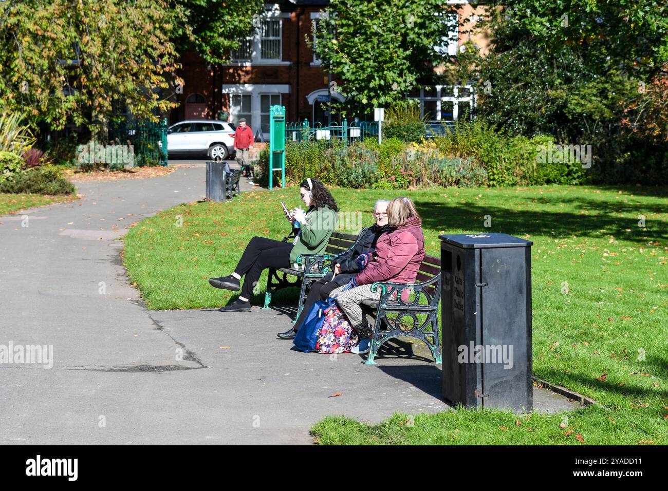 les gens assis sur les bancs du parc queens park loughborough Banque D'Images