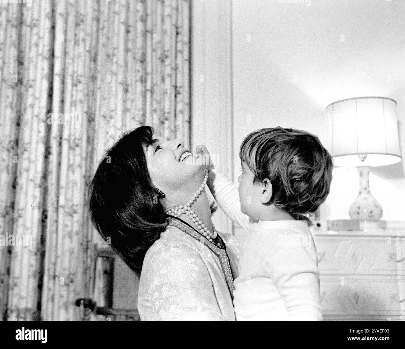 La première dame des États-Unis Jacqueline Kennedy riant alors que son fils, John F. Kennedy, Jr., joue avec son collier de perles simulées dans la pépinière de John, Maison Blanche, Washington, DC, États-Unis, Cecil Stoughton, photographies de la Maison Blanche, 27 novembre 1962 Banque D'Images