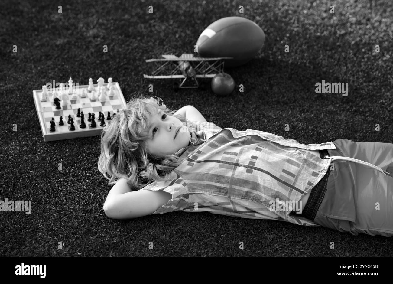 Rêve enfants et concept d'enfance. Les enfants se détendent dans le parc, pondent sur l'herbe, rêvent de jour. Un gamin pense à la pose d'échecs sur l'herbe dans le parc d'été. Le Banque D'Images