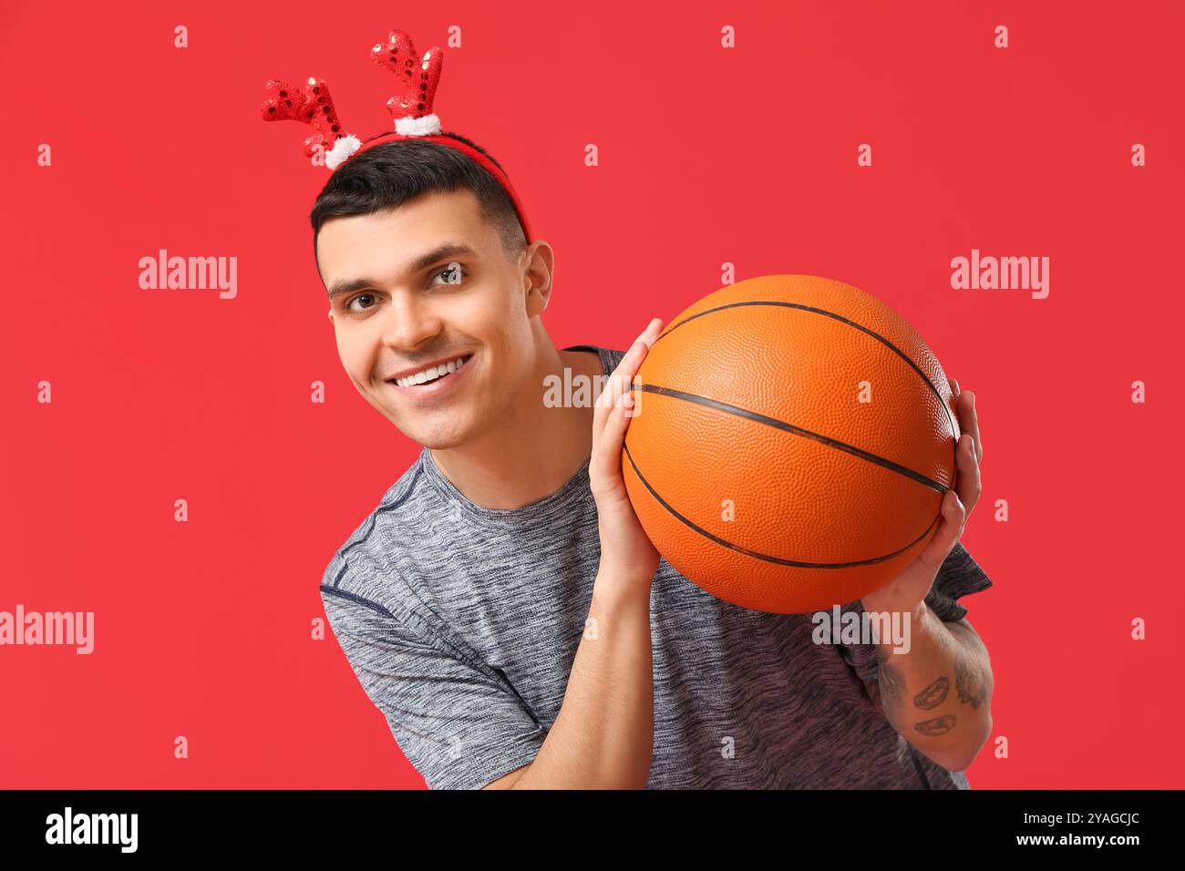 Jeune homme heureux dans des cornes de renne avec basket-ball sur fond rouge Banque D'Images