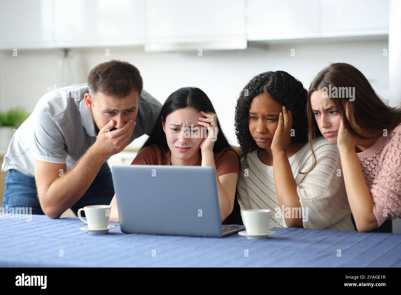 Amis interraciaux inquiets vérifiant de mauvaises nouvelles ordinateur portable dans la cuisine à la maison Banque D'Images