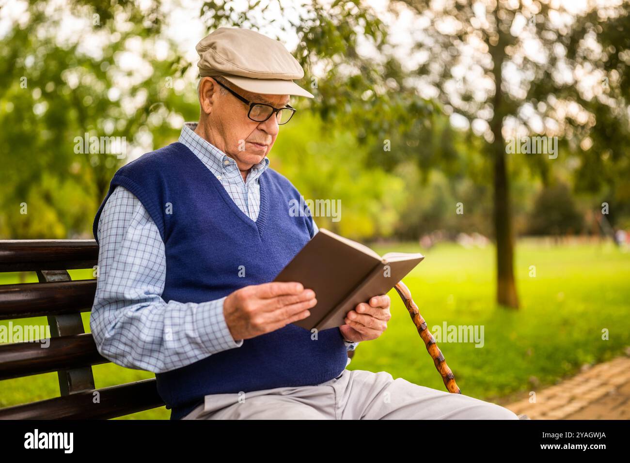 Portrait d'homme senior dans le parc. Il est assis sur un banc et lit un livre. Banque D'Images