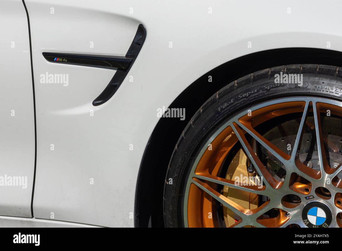 Gros plan d'une bmw m4 blanche présentant le logo emblématique de la série m et une jante en alliage de cuivre Banque D'Images