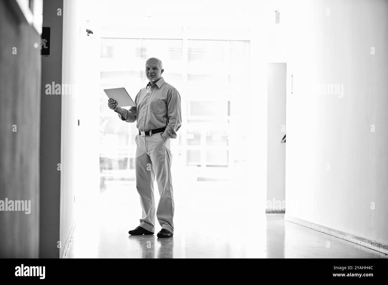 Cadre supérieur confiant dans un hall de bureau moderne tenant une tablette, mettant en valeur son expertise. Le réglage noir et blanc ajoute de l'élégance, mettant l'accent sur le succès. Repré Banque D'Images