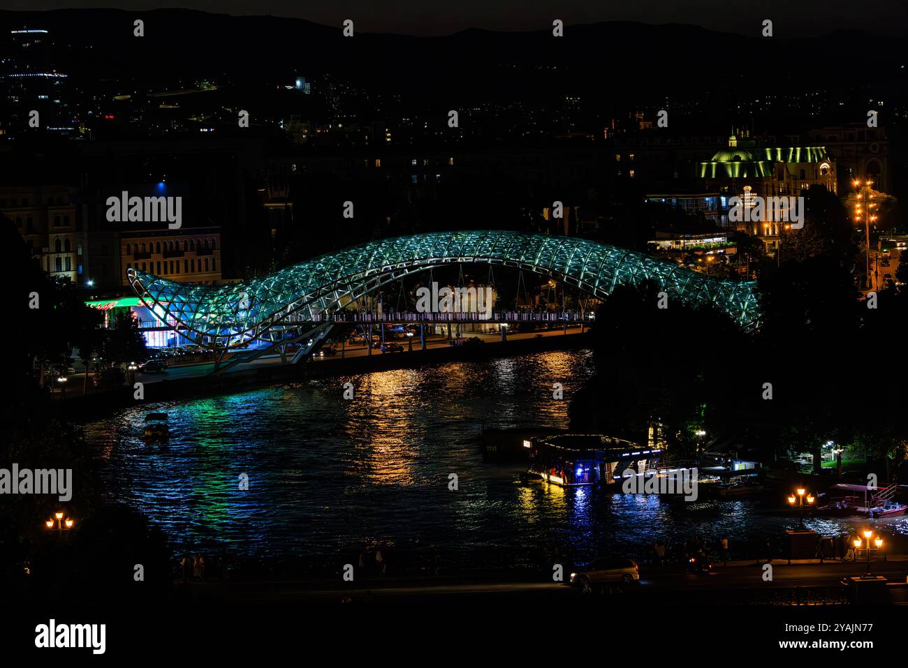 Scène nocturne regardant vers le bas l'emblématique pont de la paix illuminé et reflété dans la rivière Kura à Tbilissi géorgie Banque D'Images