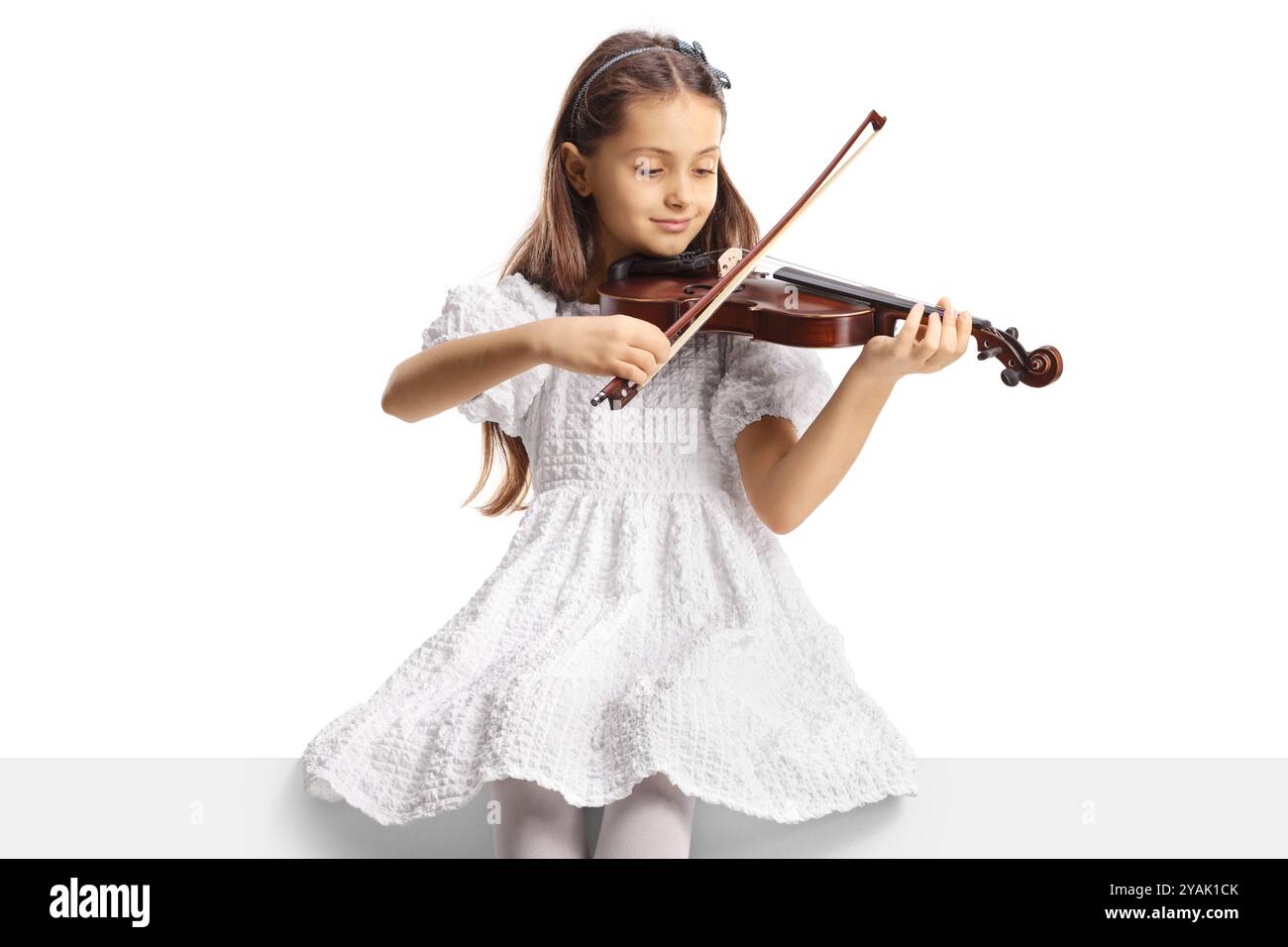 Fille dans une robe blanche assise sur un panneau blanc et jouant un violon isolé sur fond blanc Banque D'Images