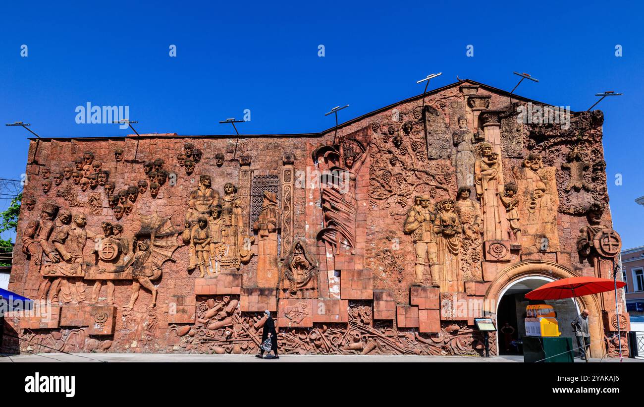 une dame locale en robe noire traditionnelle marche seule devant l'énorme murale bas relief de l'ère soviétique sur le côté de la salle de marché à kutaisi géorgie Banque D'Images