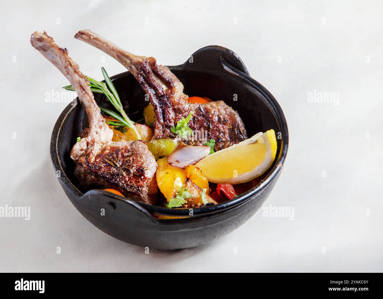 Côtes d'agneau (deux) ( un peu trop cuites) et légumes et une tranche de citron dans une assiette noire profonde sur fond blanc dans un restaurant de Washington, Banque D'Images