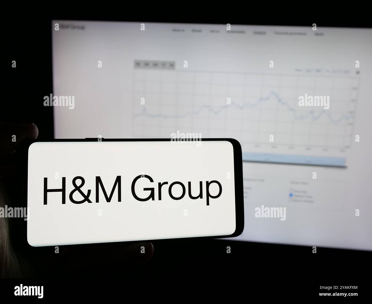 Personne tenant le téléphone portable avec le logo de la société de mode suédoise H M Hennes Mauritz AB sur l'écran en face de la page Web. Concentrez-vous sur l'affichage du téléphone. Banque D'Images