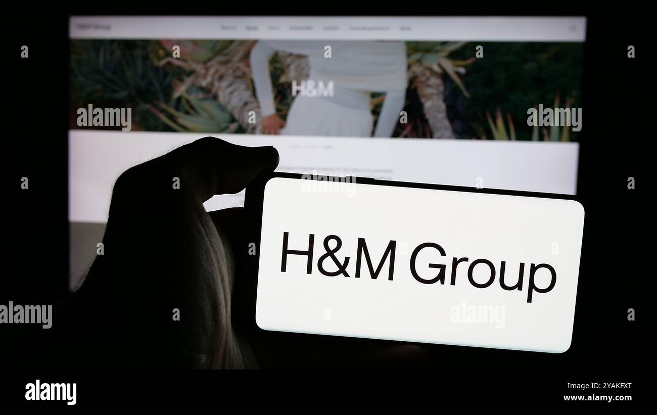 Personne tenant un smartphone avec le logo de l'entreprise de mode suédoise H M Hennes Mauritz AB sur l'écran en face du site. Concentrez-vous sur l'affichage du téléphone. Banque D'Images