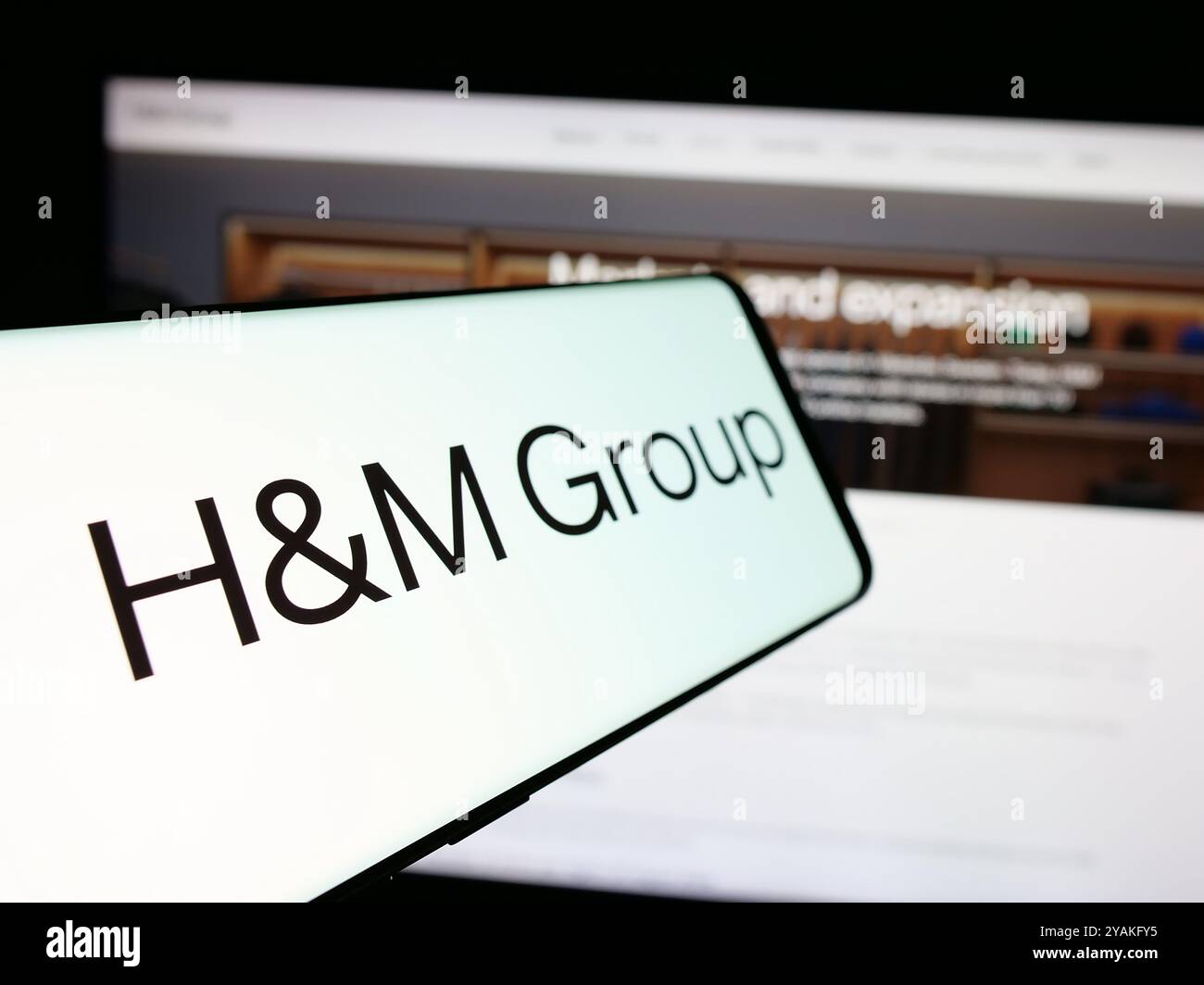 Téléphone portable avec le logo de la société de mode suédoise H M Hennes Mauritz AB sur l'écran en face du site Web. Mettez l'accent sur le centre-gauche de l'écran du téléphone. Banque D'Images