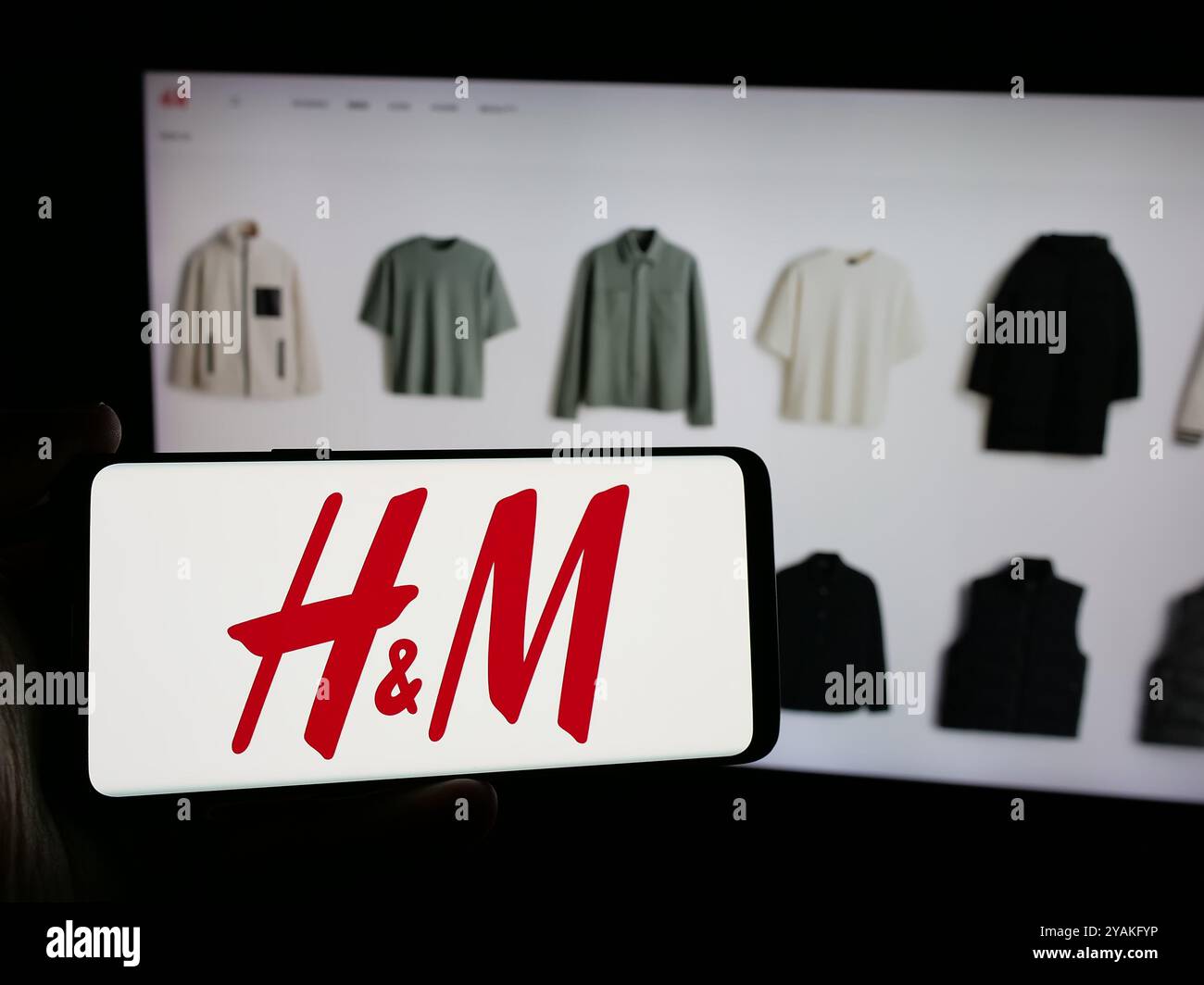 Personne tenant le téléphone portable avec le logo de la société de mode suédoise H et M (HM) sur l'écran en face de la page Web de l'entreprise. Concentrez-vous sur l'affichage du téléphone. Banque D'Images