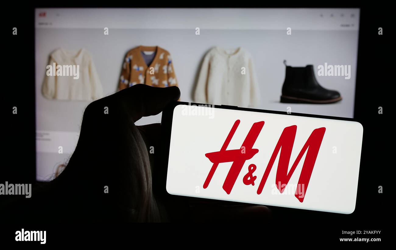 Personne tenant un smartphone avec le logo de l'entreprise de mode suédoise H et M (HM) sur l'écran en face du site Web. Concentrez-vous sur l'affichage du téléphone. Banque D'Images