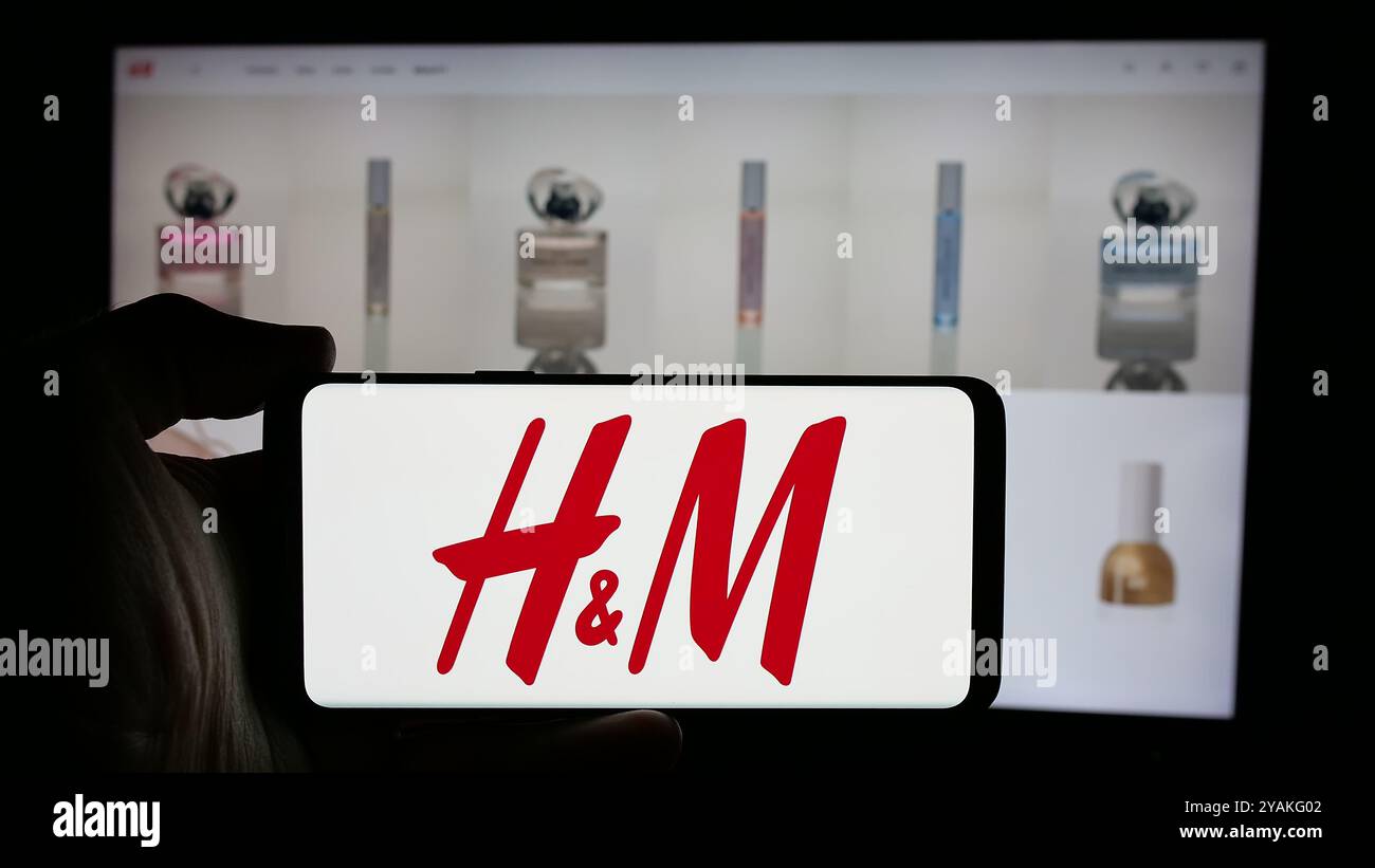 Personne tenant le téléphone portable avec le logo de la société de mode suédoise H et M (HM) sur l'écran en face de la page Web de l'entreprise. Concentrez-vous sur l'affichage du téléphone. Banque D'Images