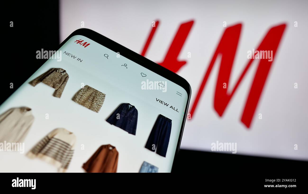 Téléphone portable avec site Web de l'entreprise de mode suédoise H et M (HM) sur l'écran devant le logo de l'entreprise. Concentrez-vous sur le coin supérieur gauche de l'écran du téléphone. Banque D'Images