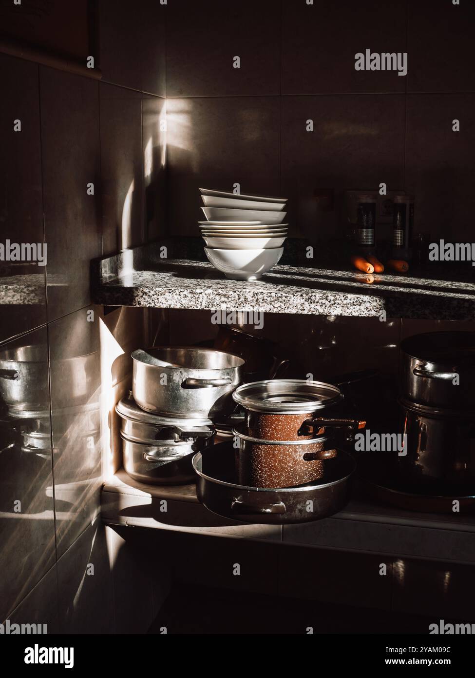 Un coin cuisine faiblement éclairé avec une lumière spectaculaire qui illumine les plats empilés, bols, casseroles et poêles. Banque D'Images