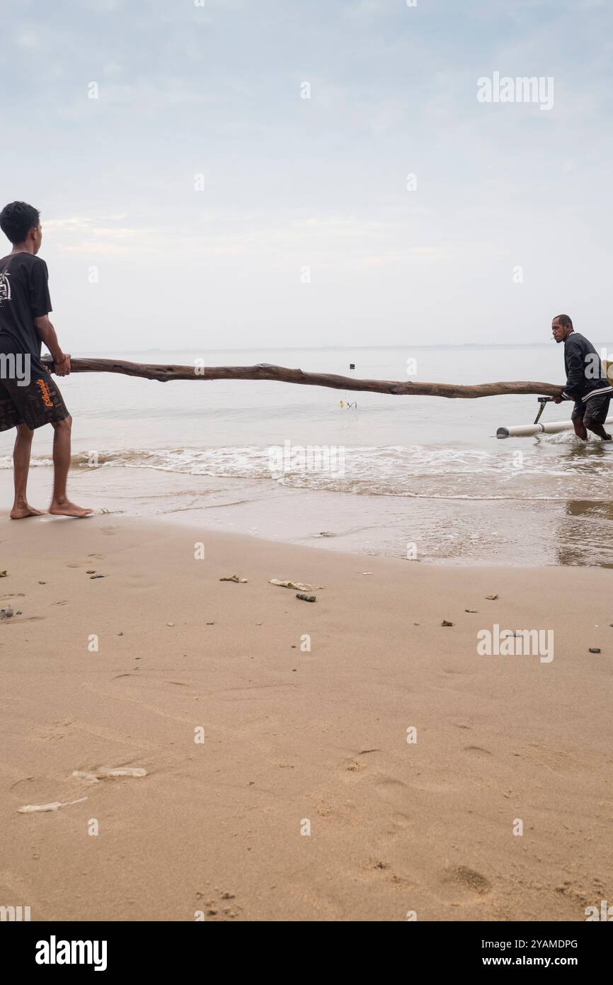 Deux personnes soulèvent une longue bûche sur la plage Banque D'Images