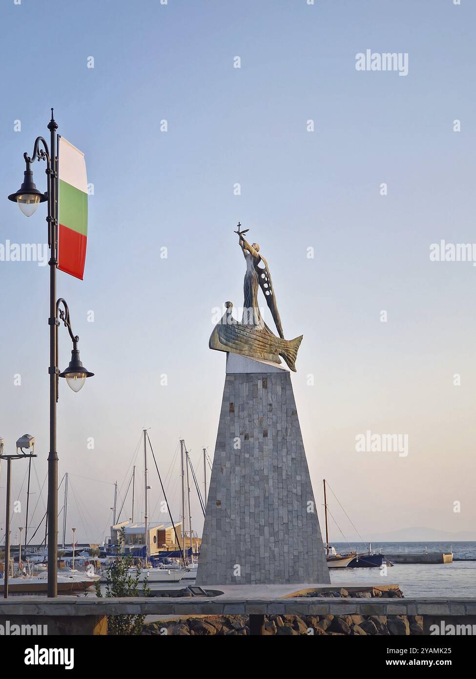 La statue de Saint Nicolas patron des marins dans la vieille ville de Nessebar, Bulgarie. Coucher de soleil serein au port avec des bateaux amarrés dans des eaux calmes, un stre Banque D'Images