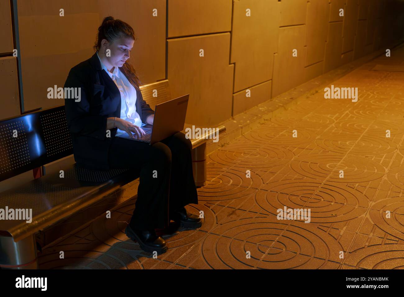 OUNG femme dans la tenue d'affaires travaillant sur ordinateur portable en attendant le train à la station de nuit Banque D'Images