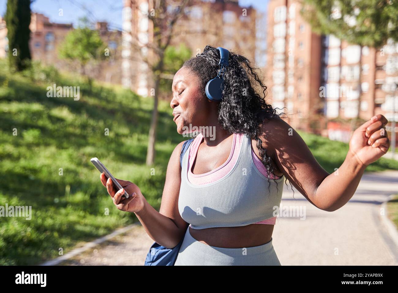 jeune femme afro-américaine sinueuse marchant avec des écouteurs sans fil écoutant de la musique et dansant Banque D'Images