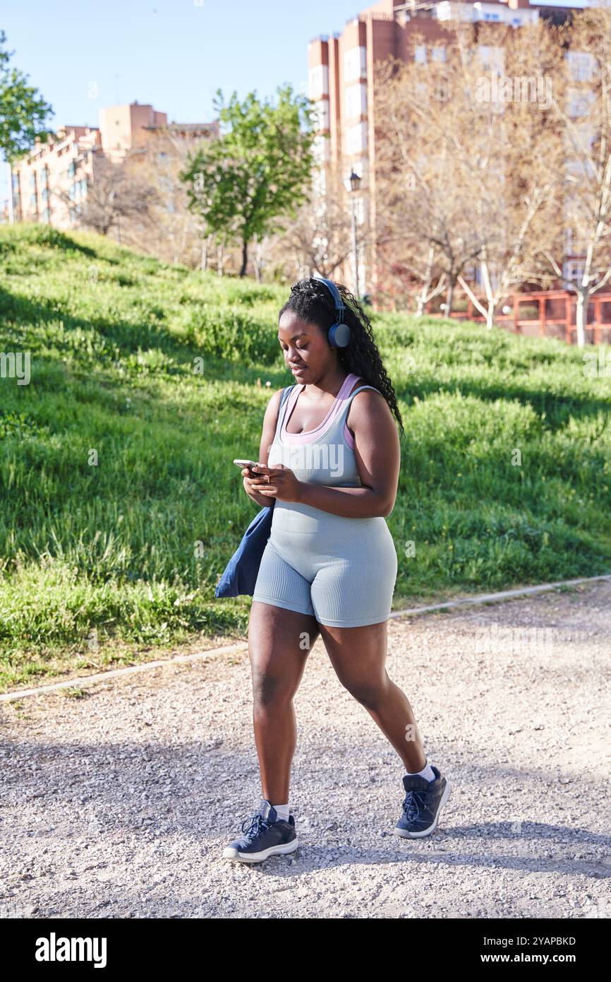 attrayant femme afro-américaine courbée marchant dans des vêtements de sport tout en utilisant son smartphone Banque D'Images
