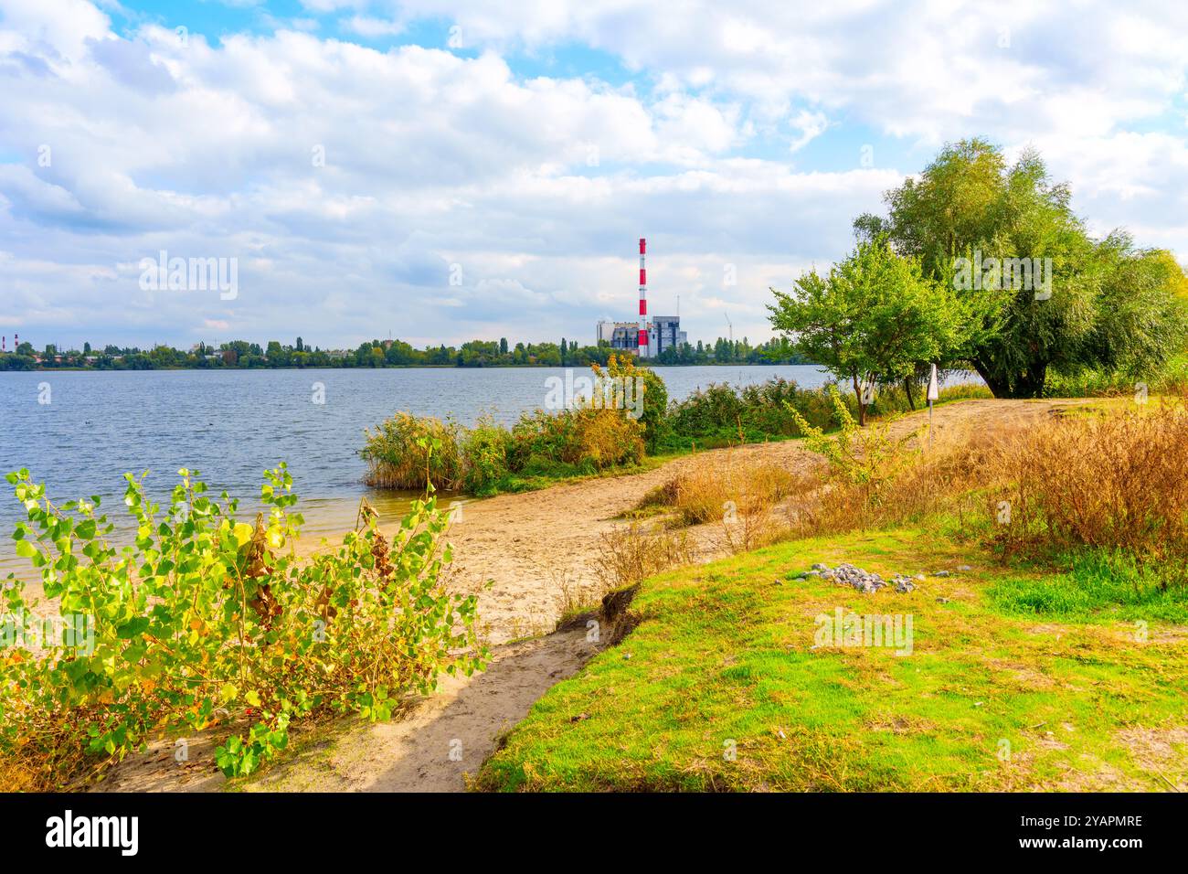 Scène au bord du lac avec plage de sable et centrale électrique industrielle en arrière-plan. Idéal pour les thèmes de la nature réunion industrie. Banque D'Images