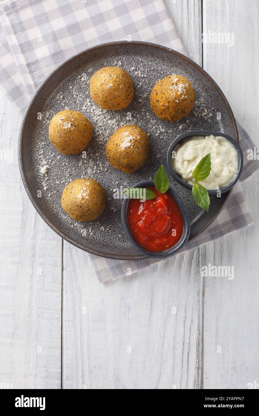 Boulettes de riz siciliennes arancini de forme conique, farcies, enrobées de chapelure et frites servies avec deux sauces gros plan dans une assiette sur un ta en bois Banque D'Images