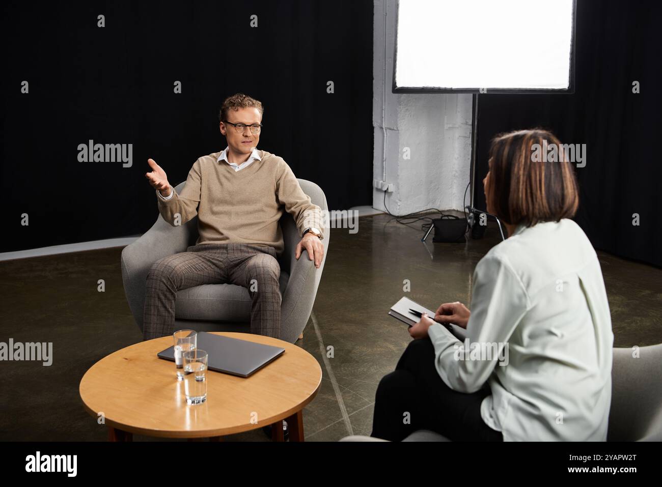 Un journaliste engage un spécialiste dans une discussion réfléchie lors d’un entretien professionnel dans un studio. Banque D'Images