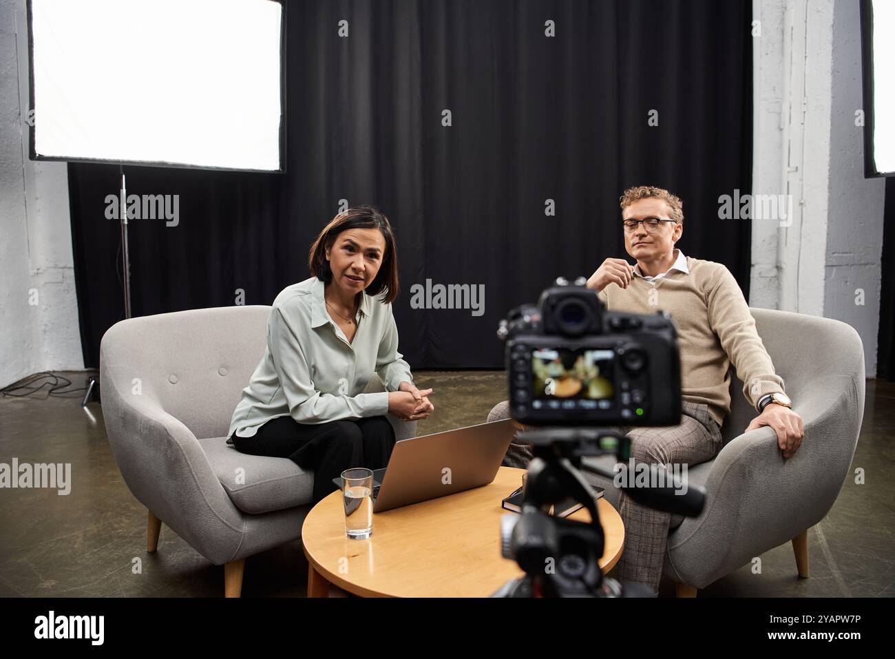 Un journaliste d'âge mûr interviewe un spécialiste masculin dans un studio élégant, capturant des dialogues perspicaces. Banque D'Images