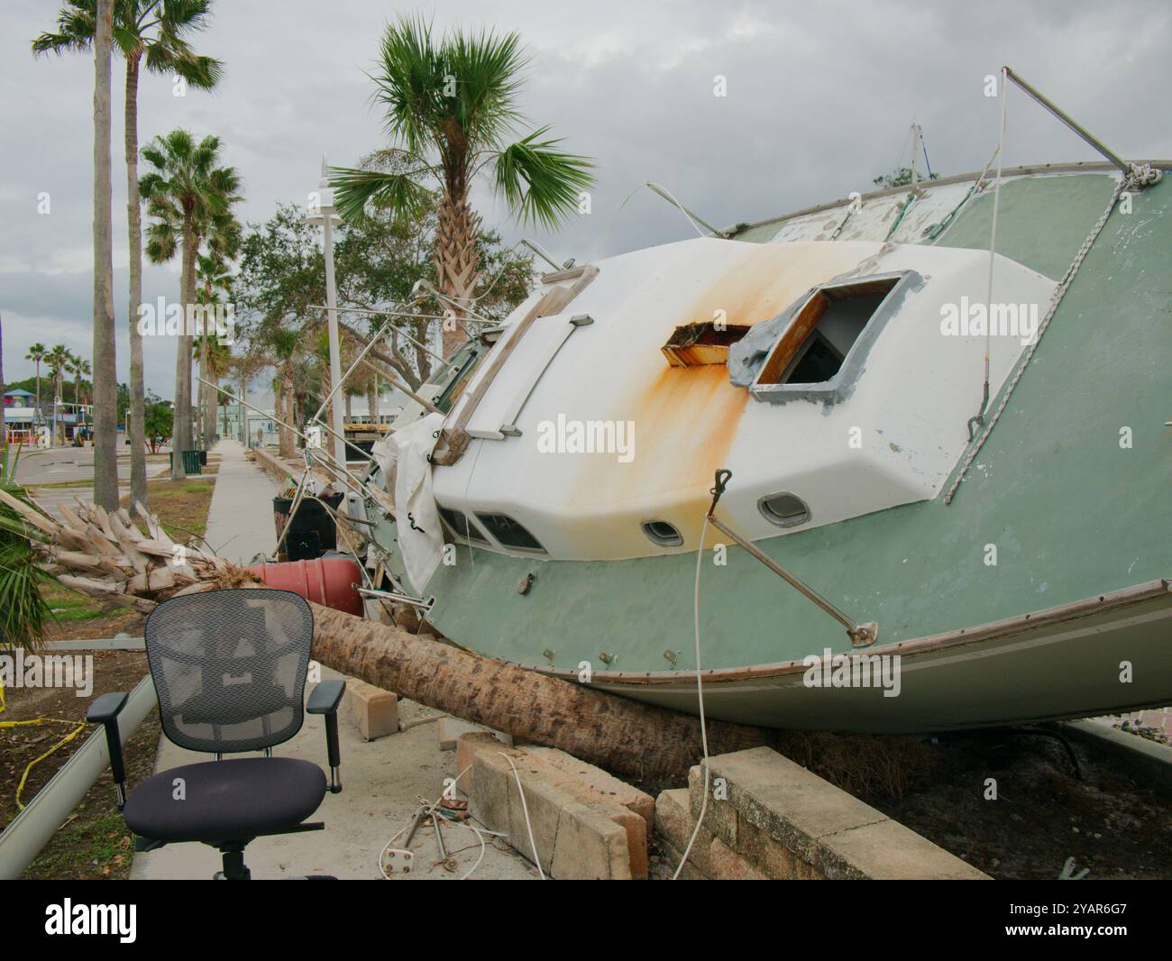 Voilier vert et blanc échoué sur le trottoir après l'onde de tempête à Gulfport, Floride. Bateau sur son côté avec des maisons en arrière-plan. Lavé Banque D'Images