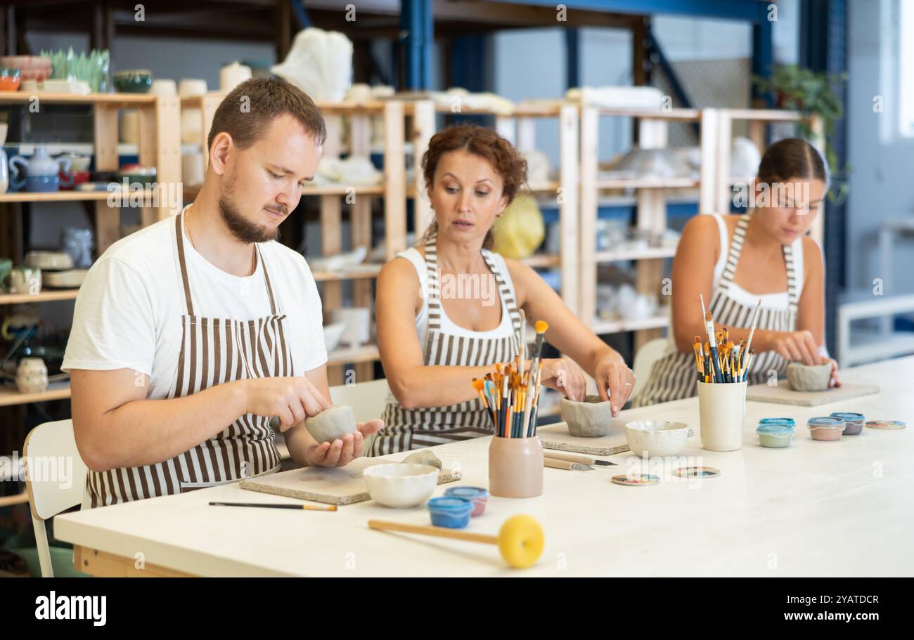 Trois étudiants en poterie moulent l'argile en assiettes faites maison et autres ustensiles Banque D'Images