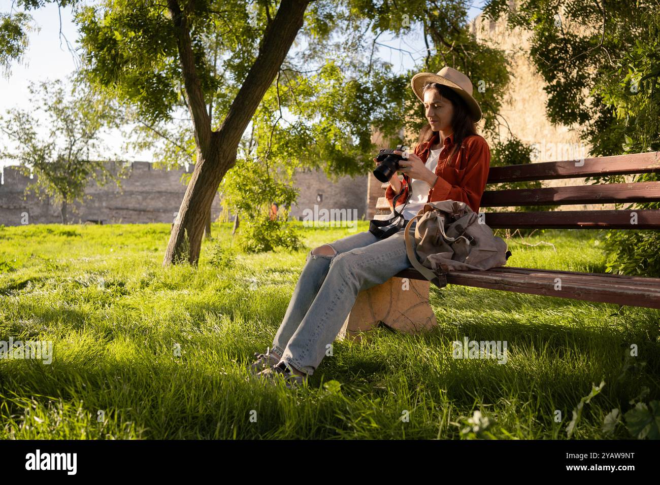 Femme touristique hispanique dans un chapeau à l'aide de la caméra et profiter du temps ensoleillé sur un banc dans le parc. Concept Relax, voyage et nature Banque D'Images