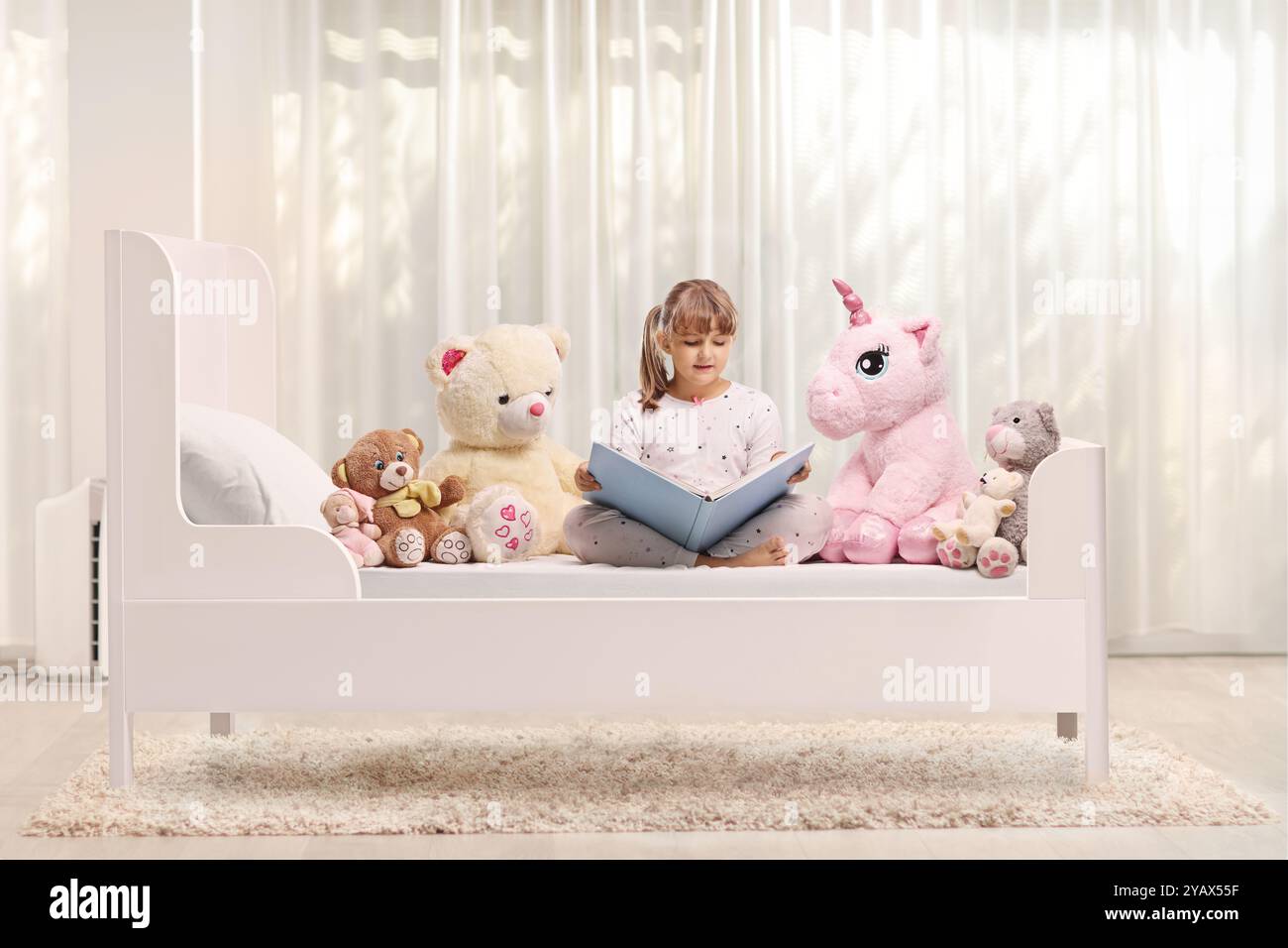 Fille assise dans un lit avec des jouets pour animaux et lisant un livre Banque D'Images