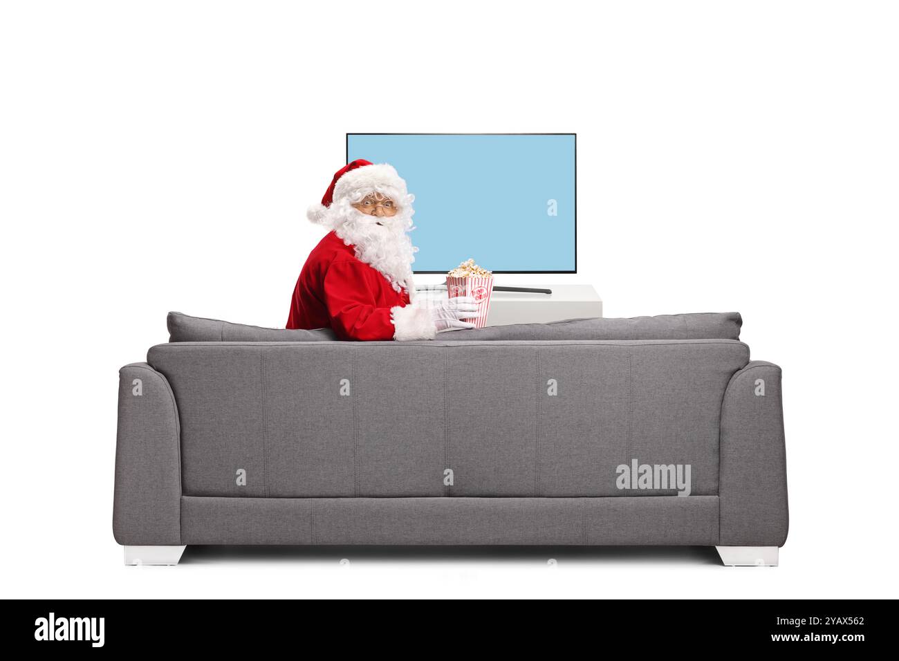 Père noël assis sur un canapé avec une boîte de pop-corn et regardant la caméra isolée sur fond blanc Banque D'Images