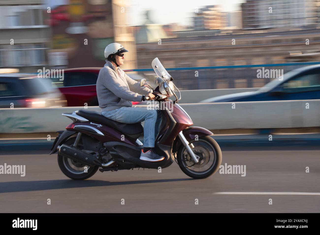 Belgrade, Serbie - 10 octobre 2024 : motocycliste mûr portant un demi-casque conduisant une moto scooter par une journée ensoleillée dans la rue de la ville Banque D'Images