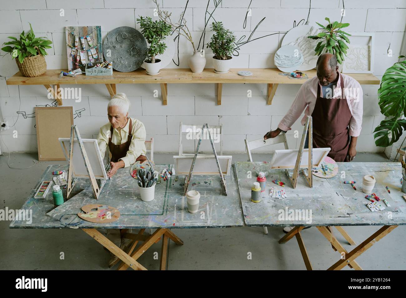 Plan à angle élevé d'artistes biraciaux seniors travaillant au bureau de travail avec des outils de peinture dans un studio de lumière rétro Banque D'Images