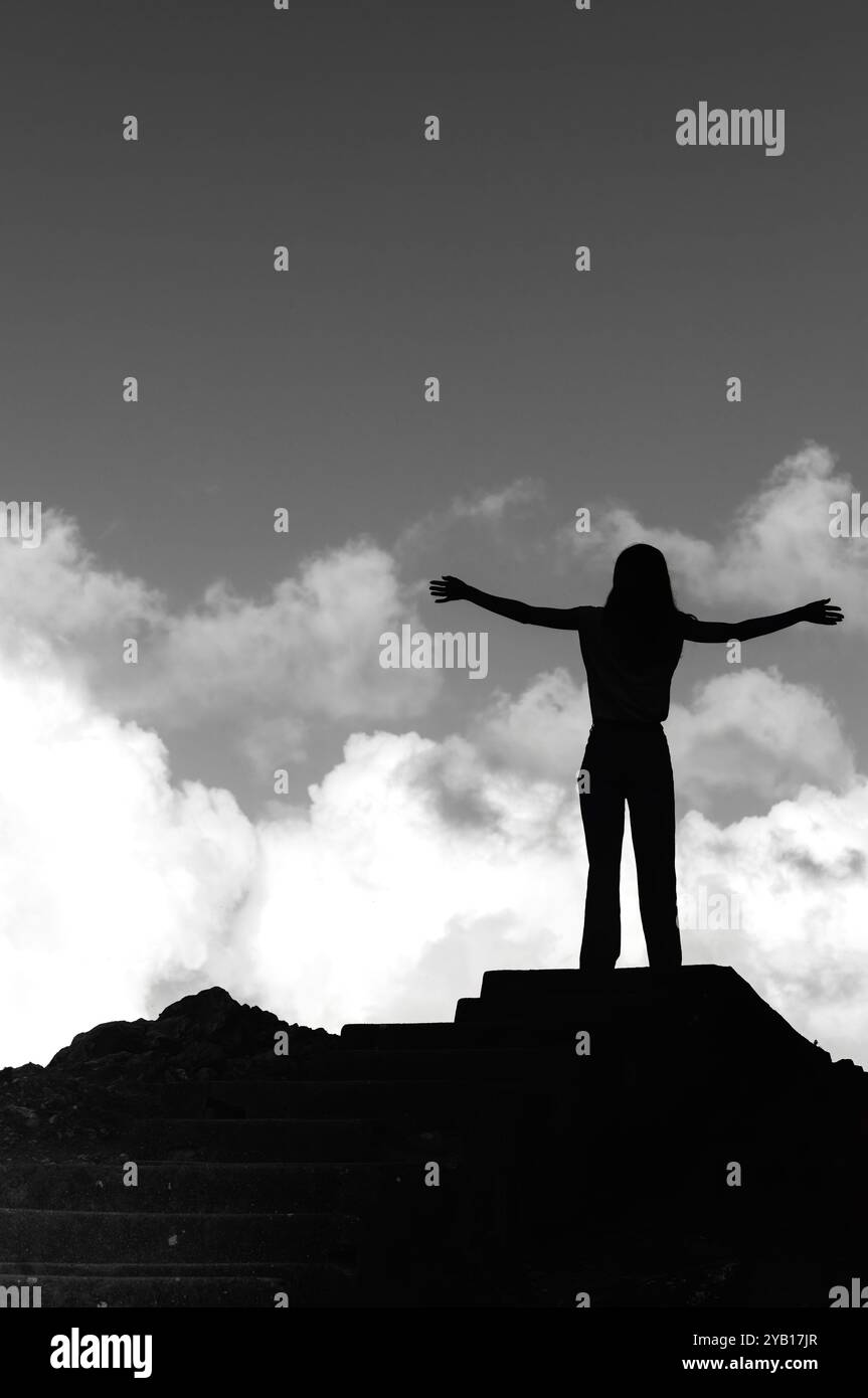 Une jeune femme se tient sur un rocher, les bras grands ouverts, embrassant l'immensité du ciel. Les nuages se dessinent au-dessus de elle alors qu'elle profite d'un moment de pure joie Banque D'Images