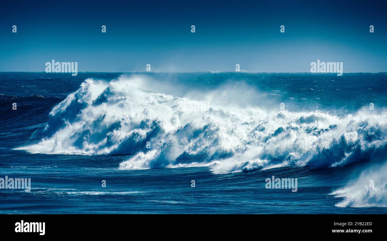 Des vagues massives se dressent et s'écrasent contre la côte rocheuse, créant une superbe exposition de mousse blanche sur fond de ciel bleu clair Banque D'Images